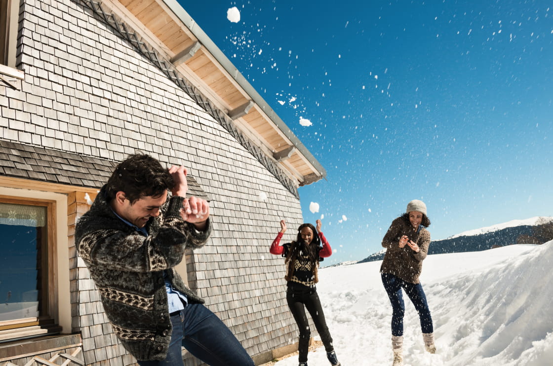 Bataille de boules de neige devant un chalet traditionnel à tavaillons