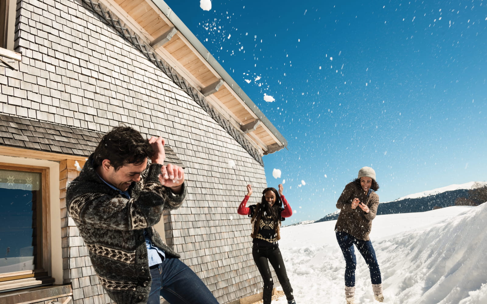 Bataille de boules de neige devant un chalet traditionnel à tavaillons