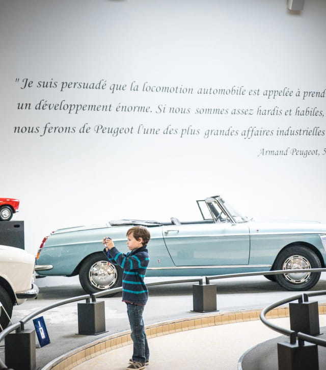Petit garçon devant une voiture de collection au musée Peugeot