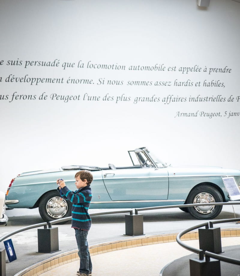 Petit garçon devant une voiture de collection au musée Peugeot
